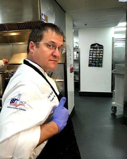 Josh Martin in his American Culinary Federation chef coat, giving a thumbs up in a commercial kitchen